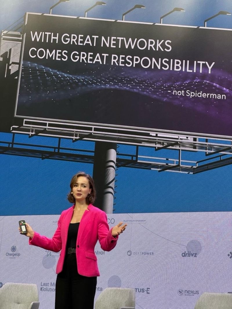 Speaker at eMobility event discussing EV-Charging networks' future, with impactful billboard in the background.