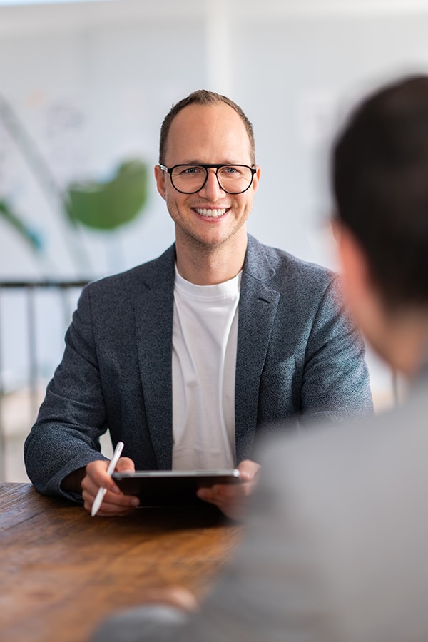 Business meeting discussing eMobility strategies. Smiling man holding tablet in a modern office setting.