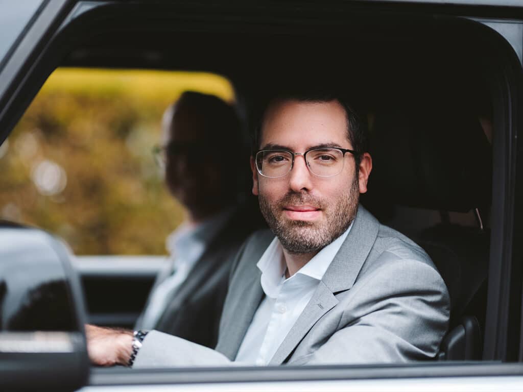 Mann im Anzug, der aus einem Auto heraus lächelt und damit Vertrauen in die Zukunft der Mobilität symbolisiert.