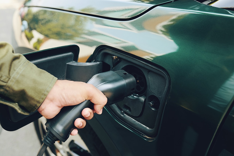 EV-Ladevorgang, Hervorhebung von eMobility und der Zukunft der Mobilität durch Hand, die Elektroauto-Ladegerät einsteckt.