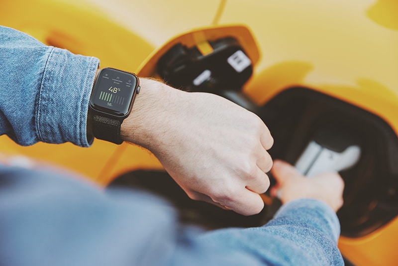 Person checking smartwatch while charging electric car, symbolizing eMobility and the future of mobility.